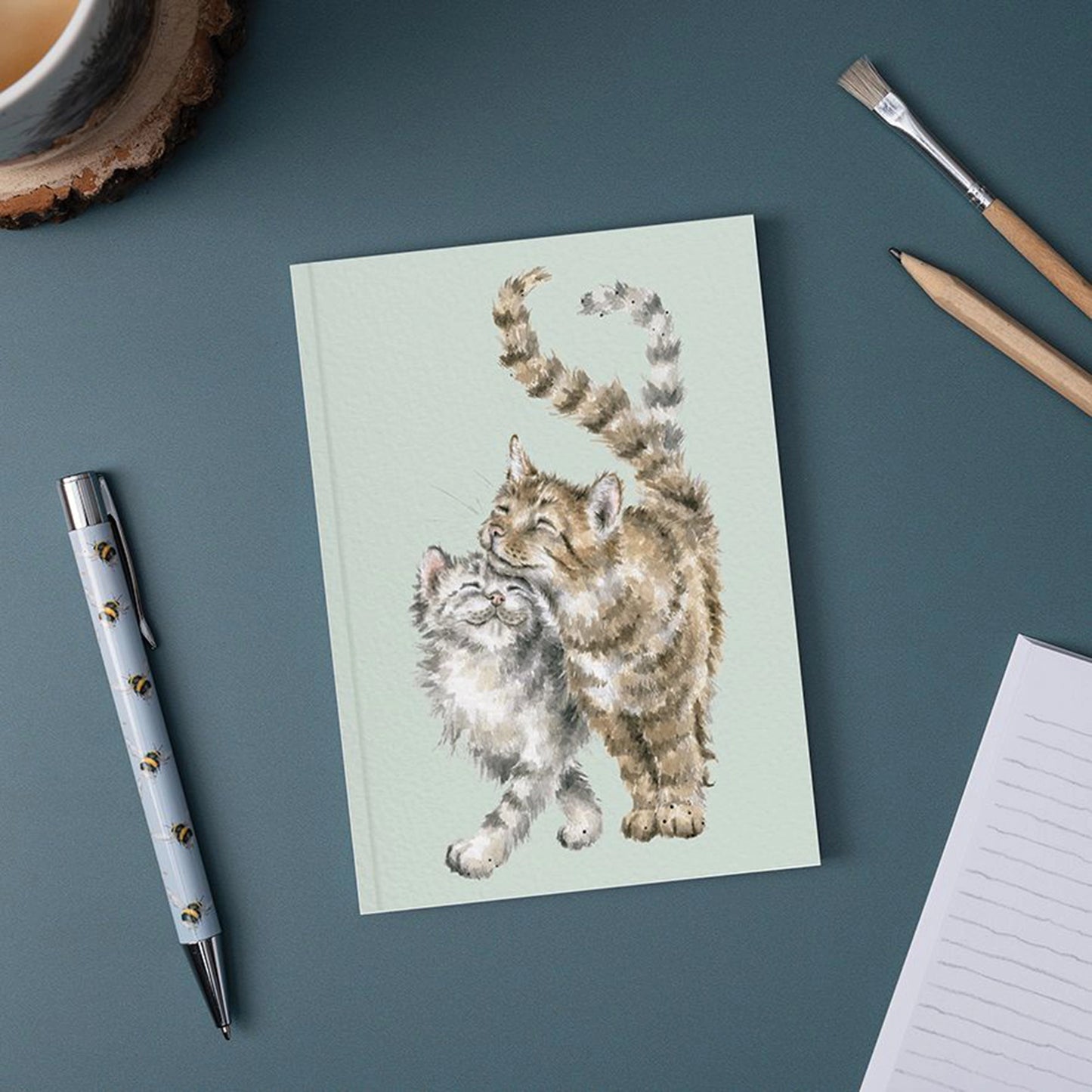 A green paper notebook featuring an illustration of two cuddling tabby cats lifestyle
