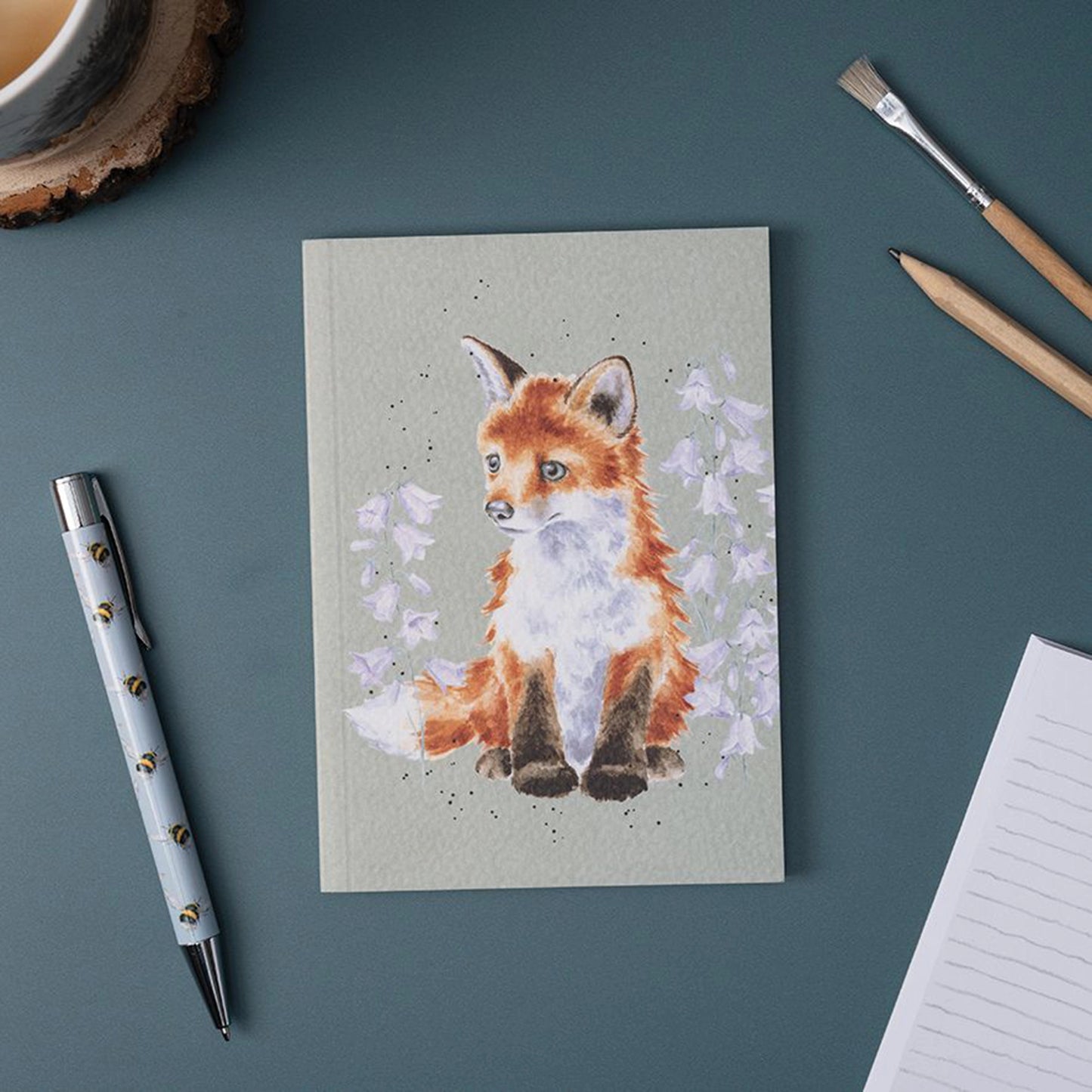 A green paper notebook featuring an illustration of a thinking fox in flowers lifestyle