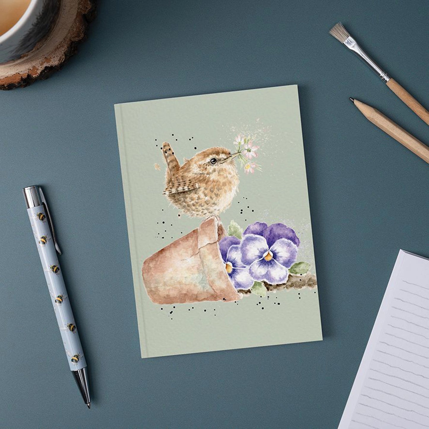 A green paper notebook featuring an illustration of little wren bird on a plant pot lifestyle