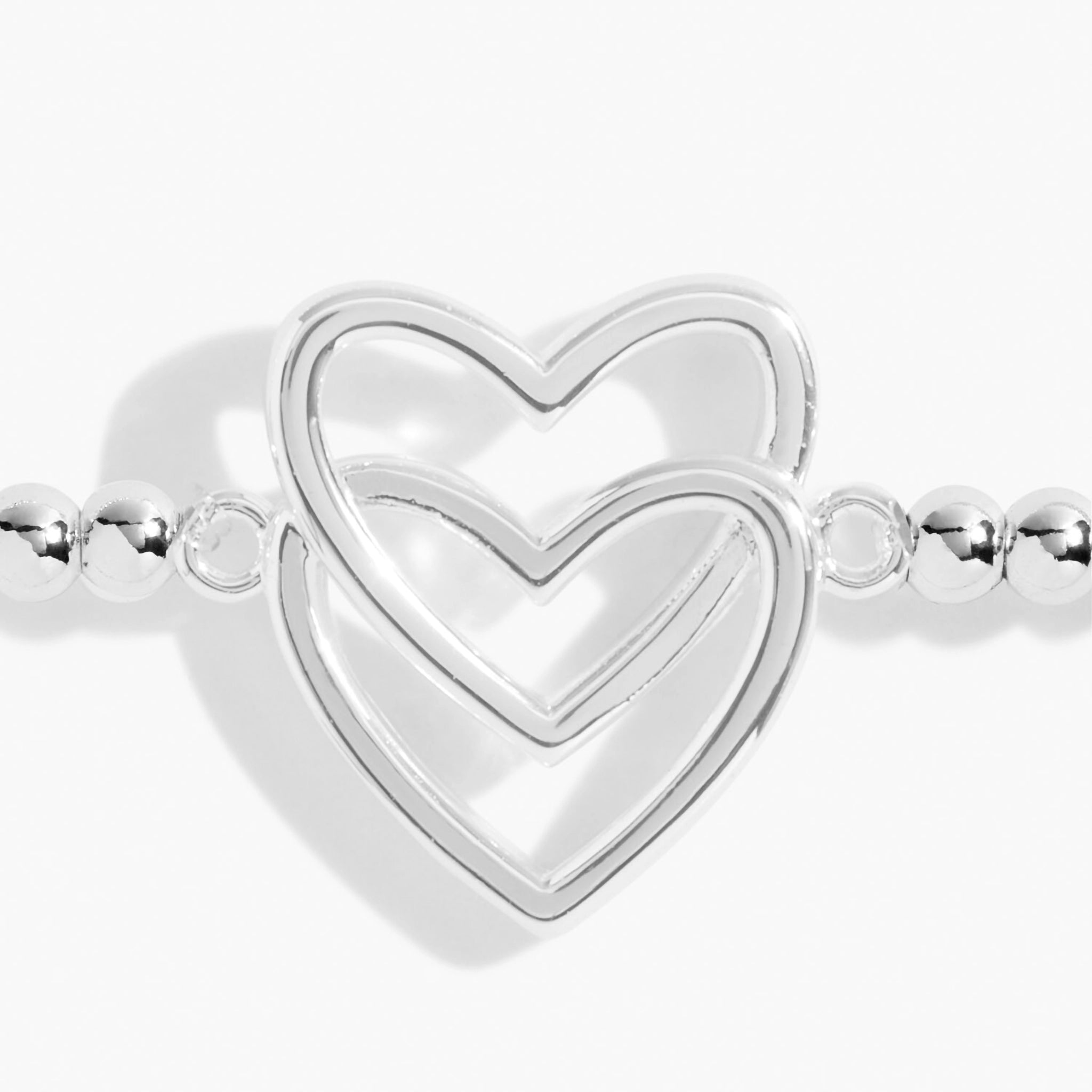 Detail of a silver beaded bracelet with two stacked silver interlinking hearts