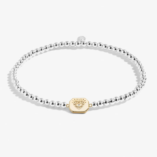 A silver beaded bracelet with a gold pendant engraved with an eye in a heart with a CZ stone