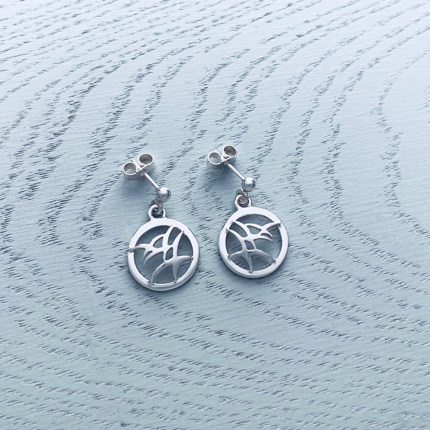 A pair of silver drop earrings with flying birds in round frames and stud post fittings