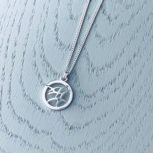 A silver necklace with a pendant featuring a flock of flying birds with a round frame design