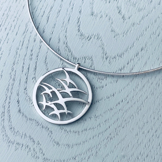 A silver necklet with a wire and a pendant featuring a flock of flying birds design in a round frame