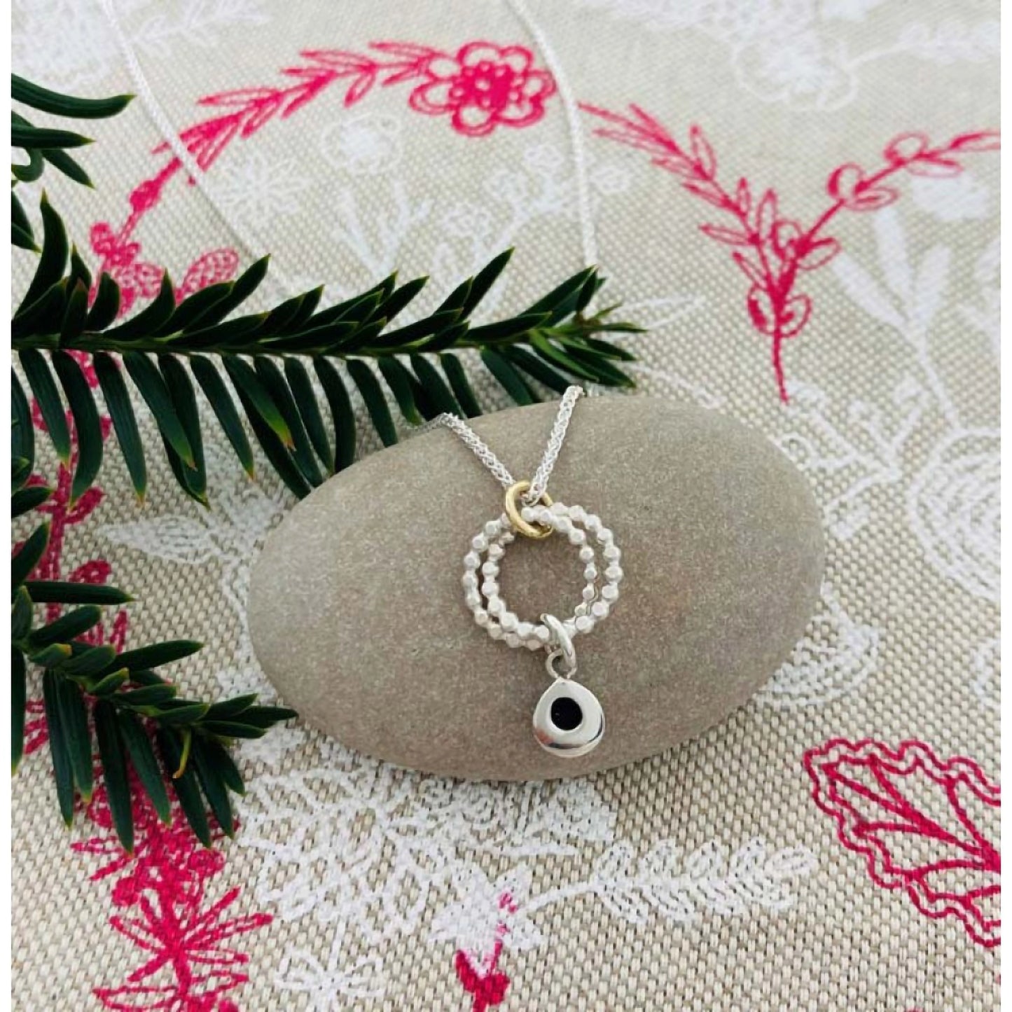 A silver pendant featuring two rings of circles and a dangling silver teardrop lifestyle image