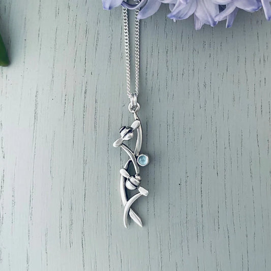 Silver necklace featuring a pendant with two bees in tall grass and a round blue topaz stone