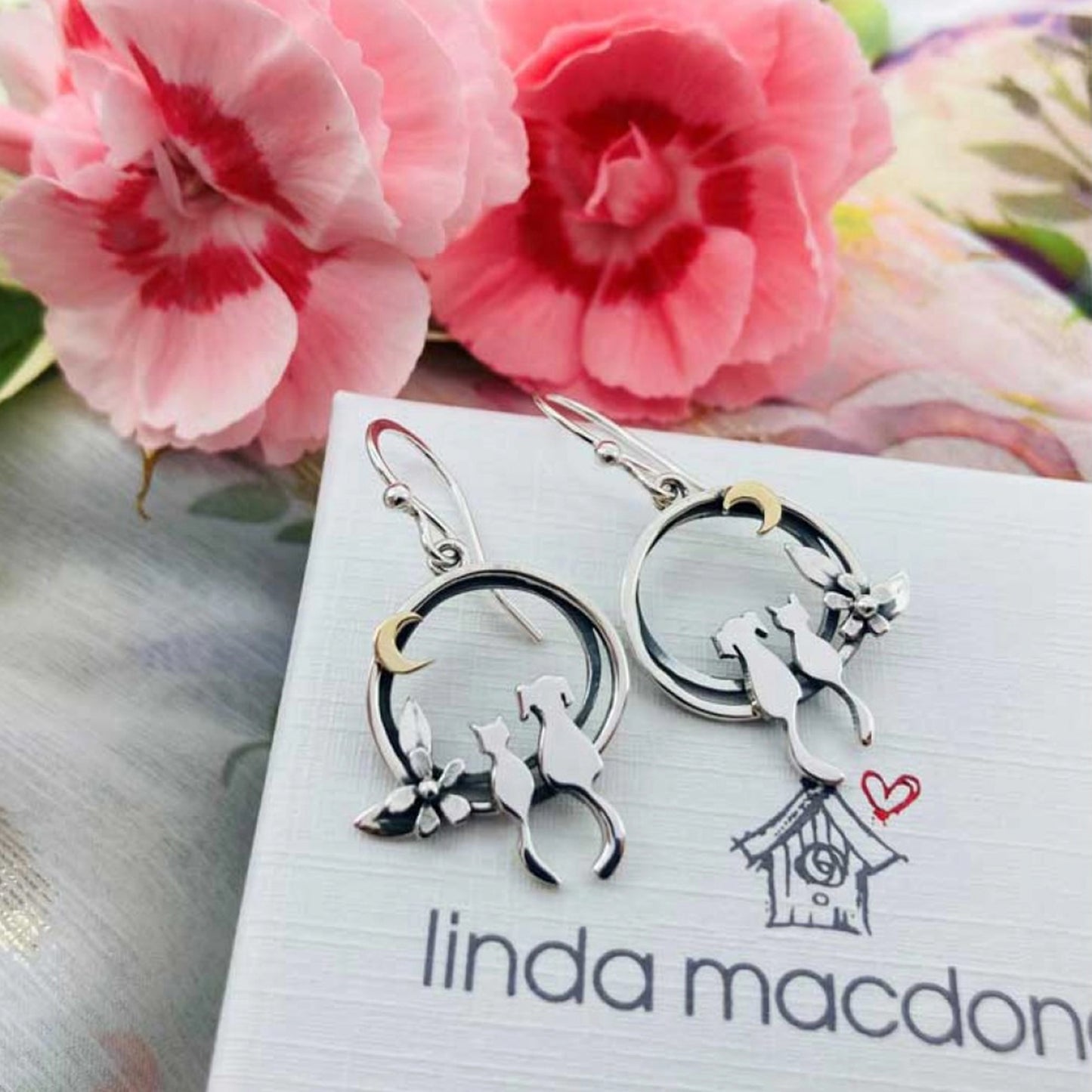 A pair of silver earrings featuring a cat and dog sat together under a gold moon