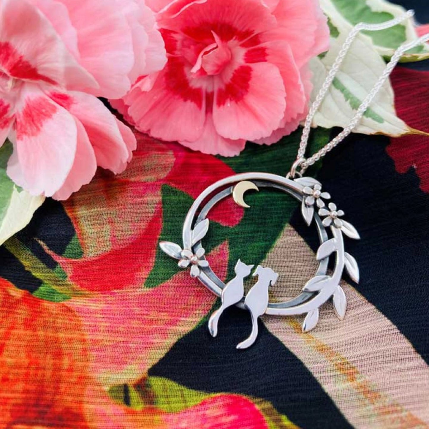 A large silver pendant featuring a cat and dog sat together under a gold moon