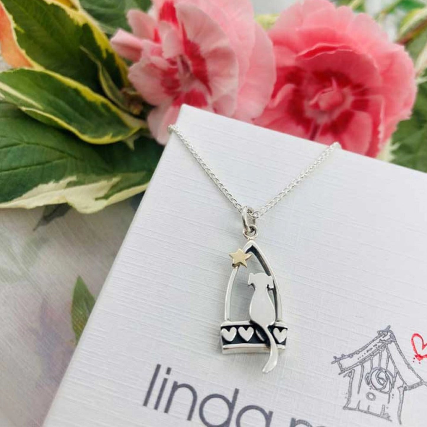 A silver stirrup pendant with a little dog, heart details and a gold star on box