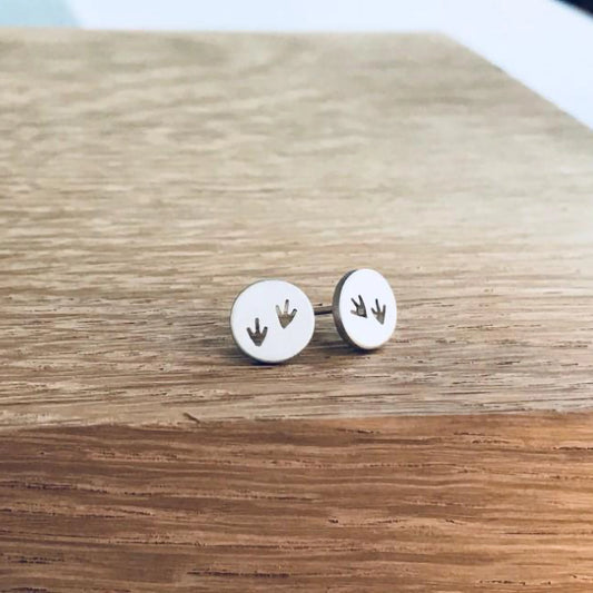 A pair of round silver studs featuring two pairs of cut-out bird prints