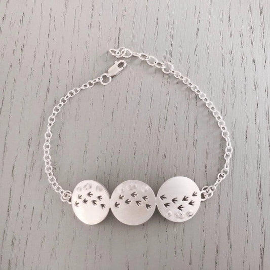 A silver bracelet with three round pendants with matt texture and a row of cut out bird prints