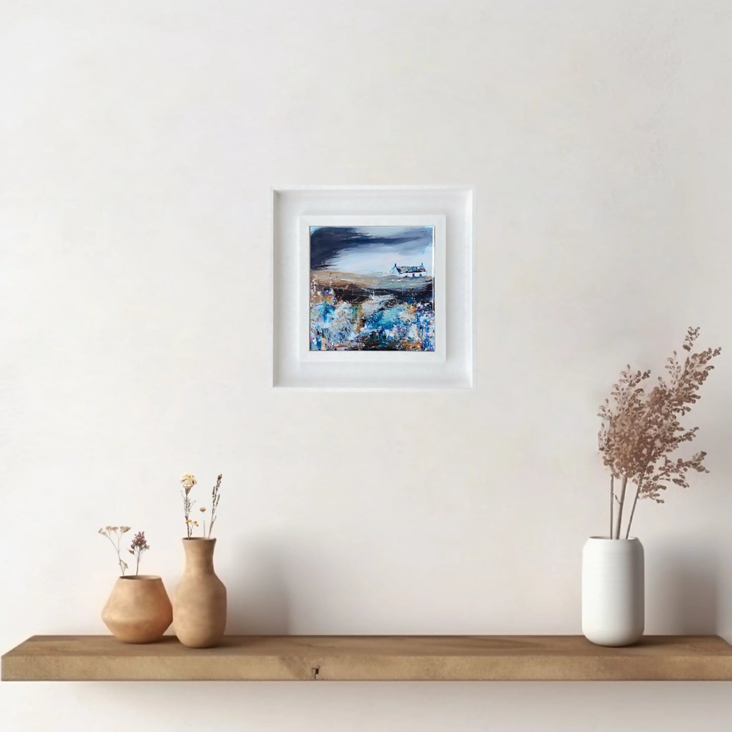A ceramic tile printed with an abstract painting of a cottage and flowers mounted on a white frame hanging