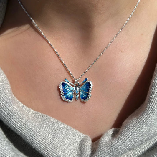 Polished silver butterfly pendant with blue enamel and silver chain on model