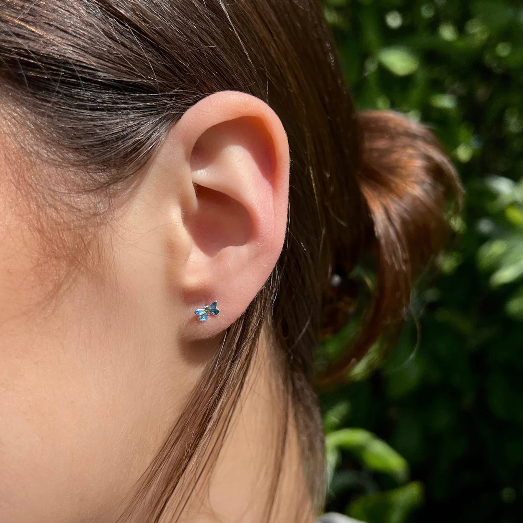 Model wearing a pair of tiny blue enamel butterfly stud earrings in polished silver