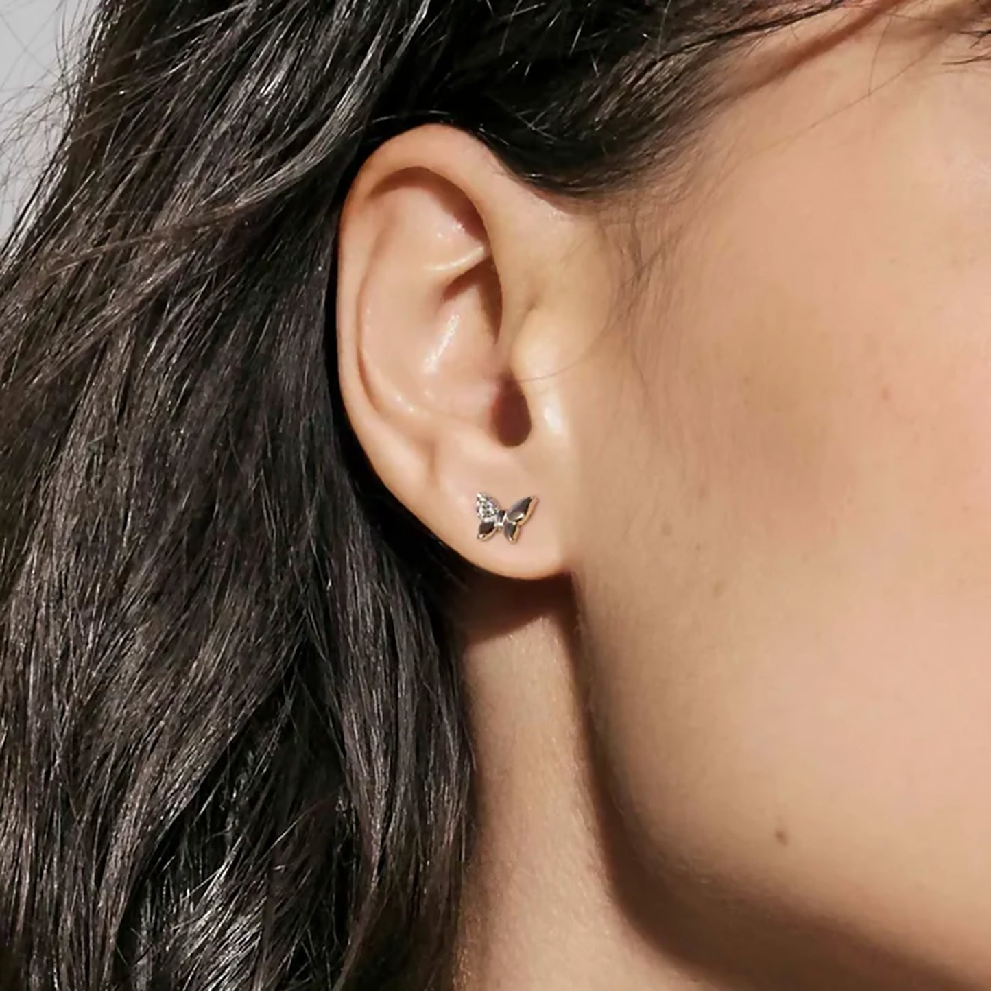 Model wearing butterfly shaped silver stud earrings with pave CZ cluster on one wing