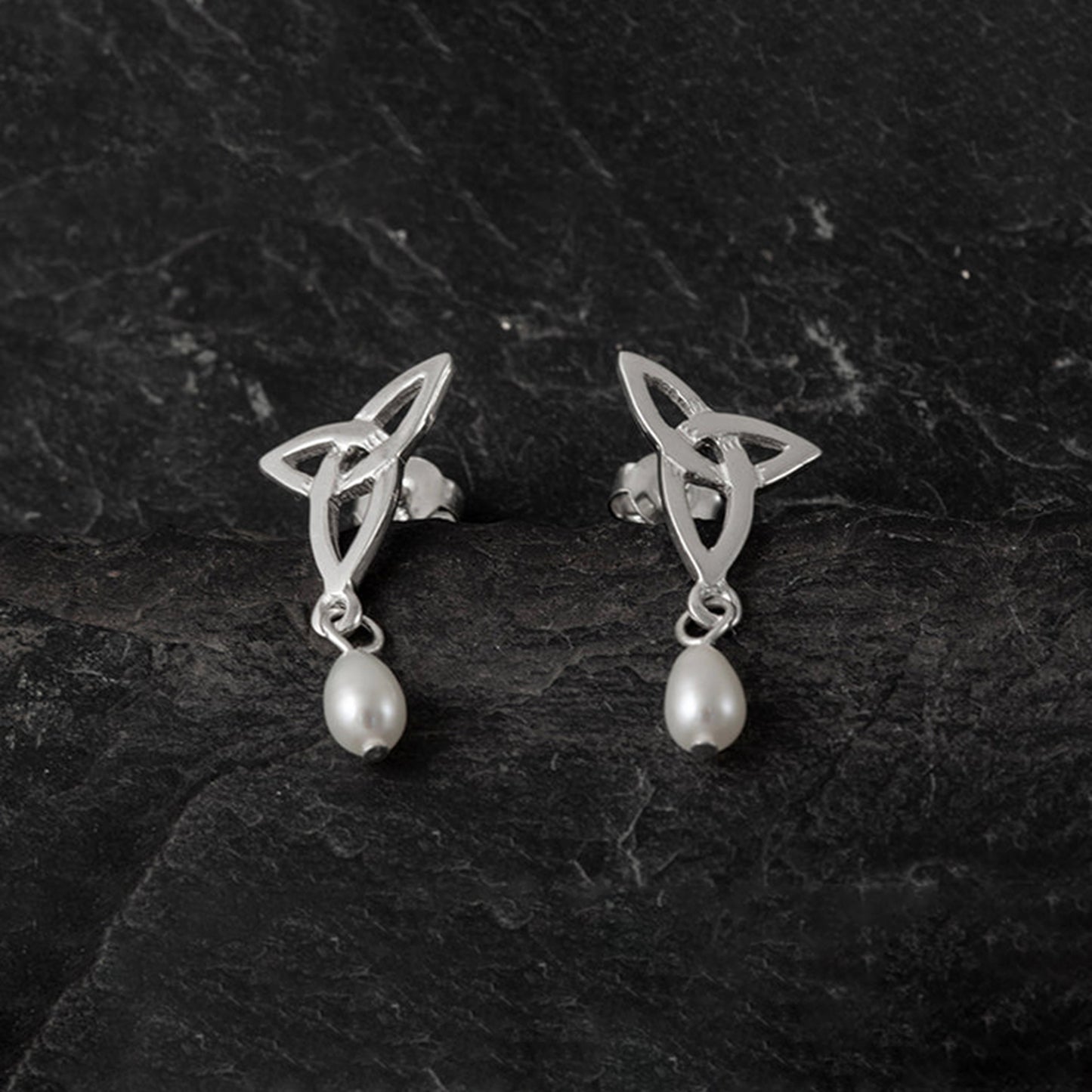 A pair of silver trinity knot shaped stud earrings with dangling white teardrop pearls