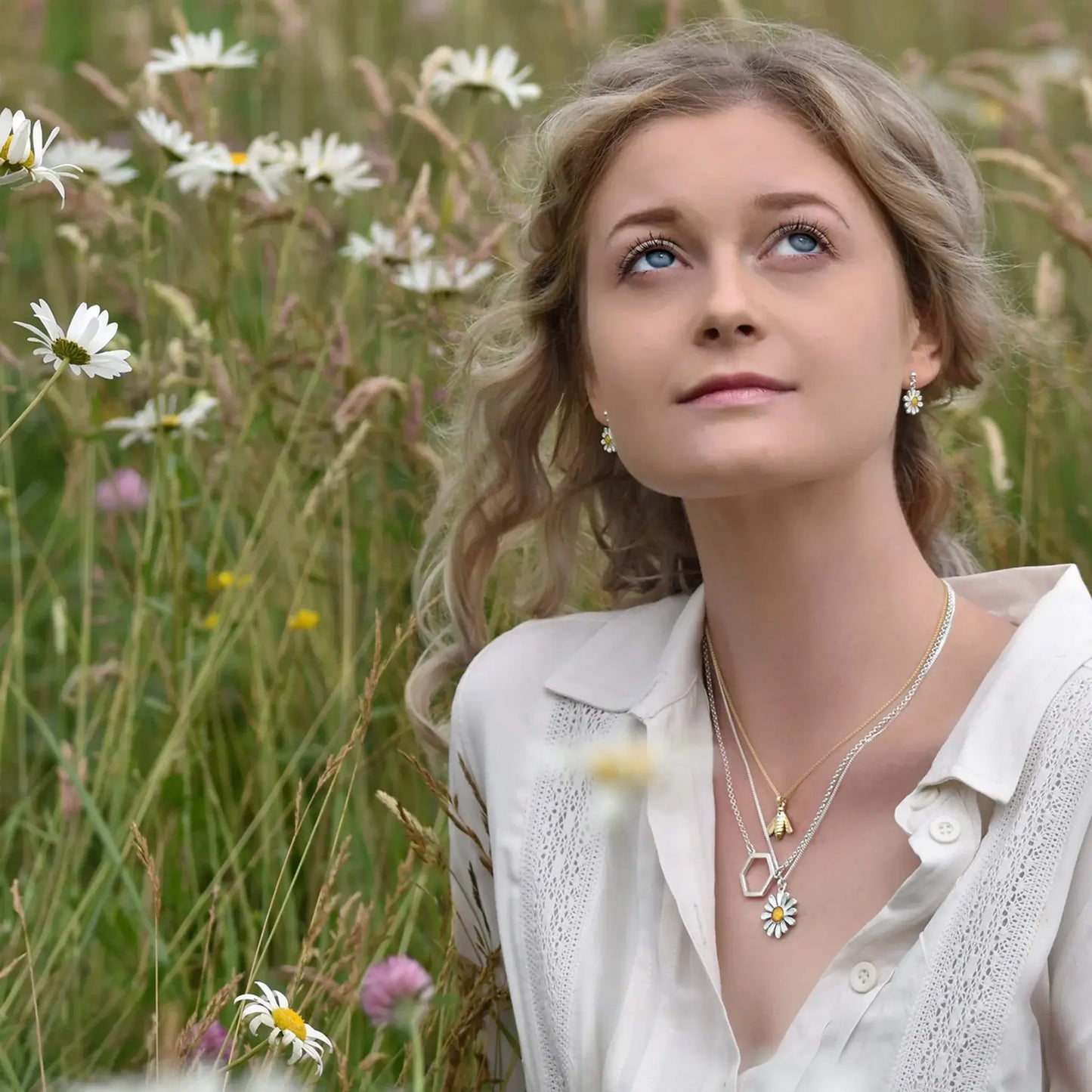 Model wearing a silver daisy pendant in yellow and white enamel with a silver chain layered with honeybee pieces