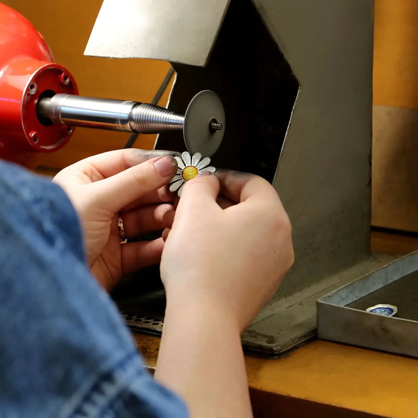 Jewellery crafter polishing up a large silver daisy pendant with yellow and white enamel