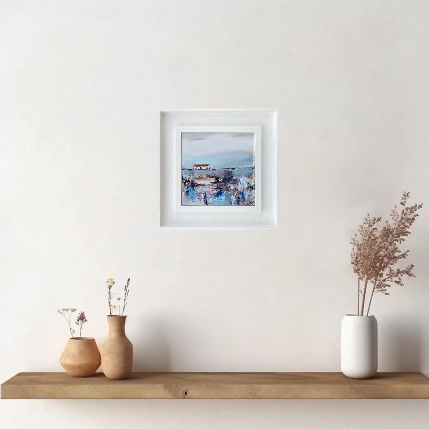 A ceramic tile printed with an abstract painting of a cottage and daisy flowers mounted on a white frame
