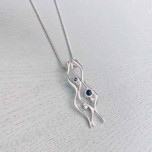 A silver pendant featuring three long ripples design with two blue topaz stones