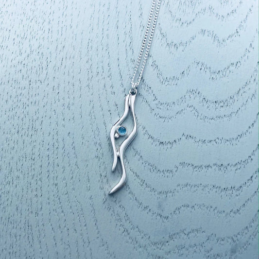 A silver pendant featuring two ripple shapes with a blue topaz stone in the centre 