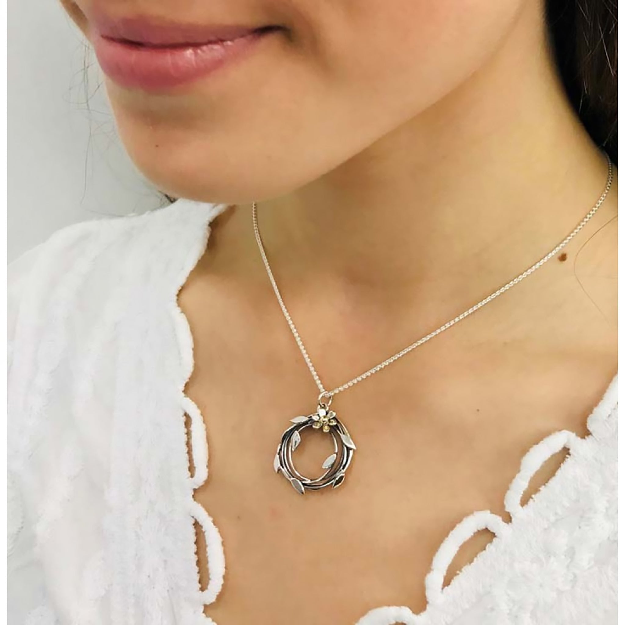 Model wearing large round woven vine wreath shaped pendant with leaf details and a flower with gold centre