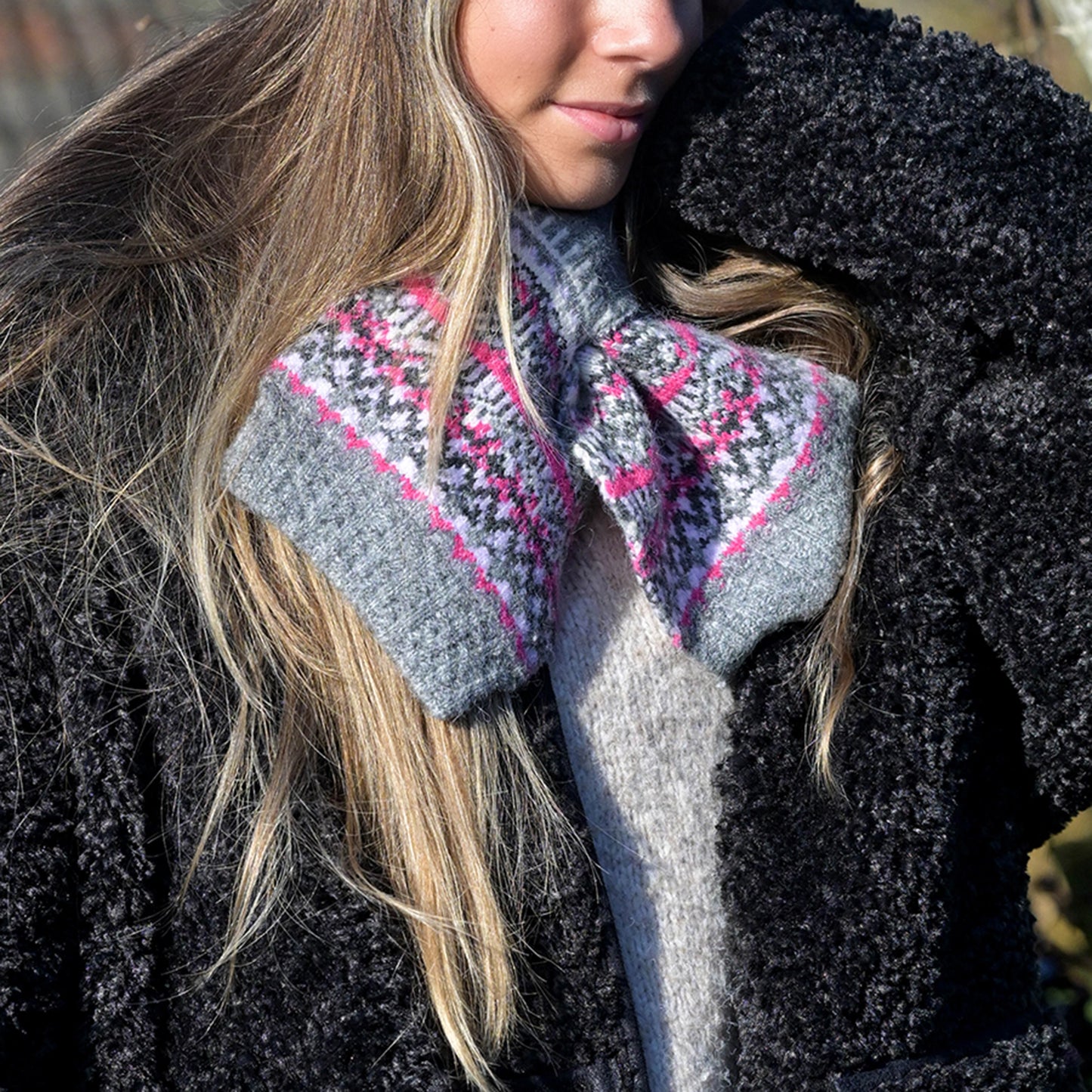 Model wearing a knitted grey pull through scarf with pink fair isle pattern