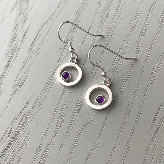 A pair of silver drop earrings featuring round frames with amethyst stones in the centre
