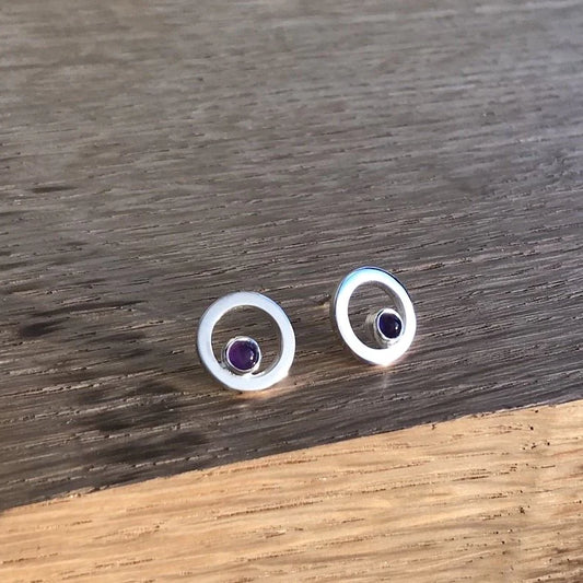 A pair of round frame silver stud earrings with amethyst stones in the centre