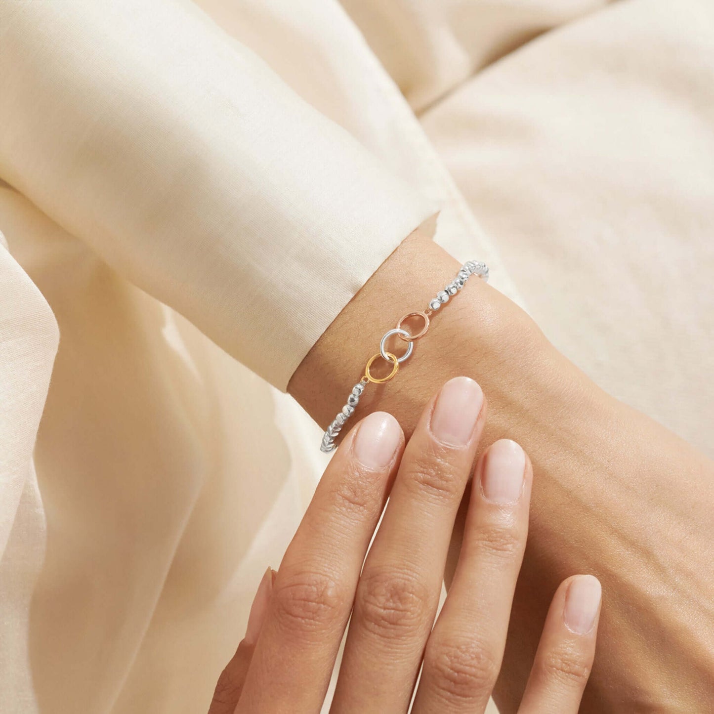 Model wearing silver bracelet with three interlinked circles in silver and two toned gold