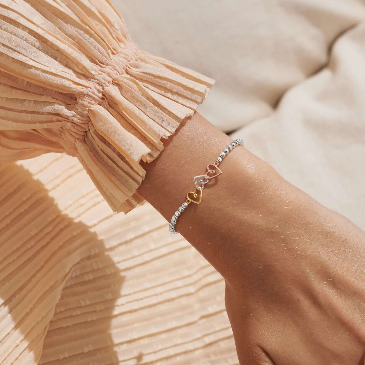 Model wearing silver bracelet with three interlinked hearts in silver and two toned gold