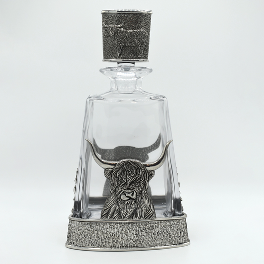 A glass decanter with pewter base featuring a Highland cow, and matching pewter stopper