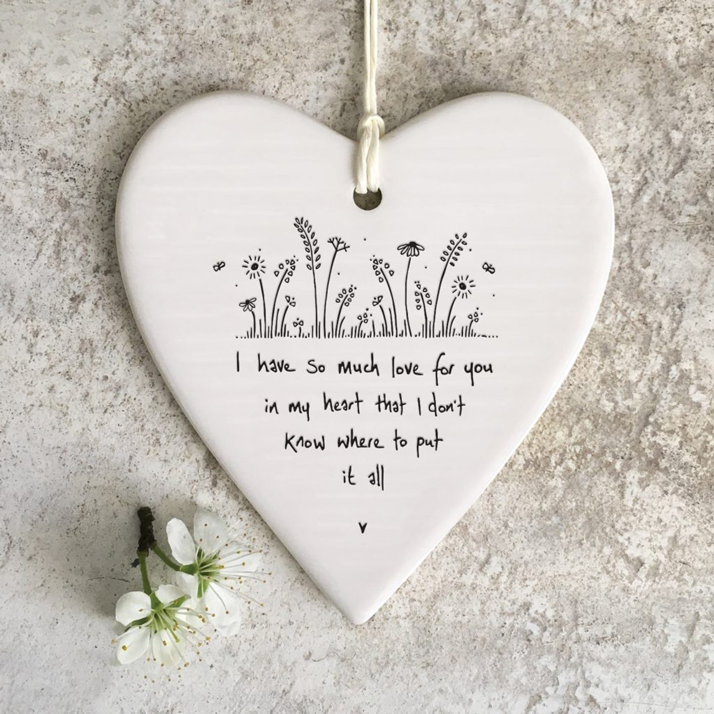 White ceramic heart with a flowers and grass illustration and a quote