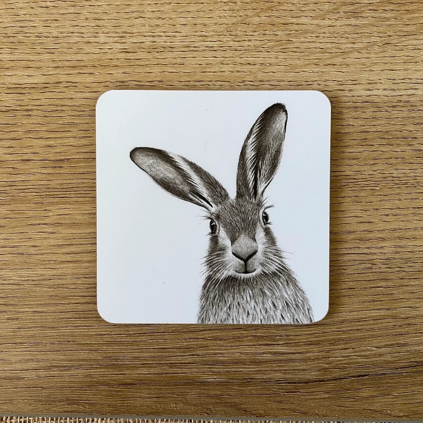 Square white coaster with a printed grayscale image of a hare