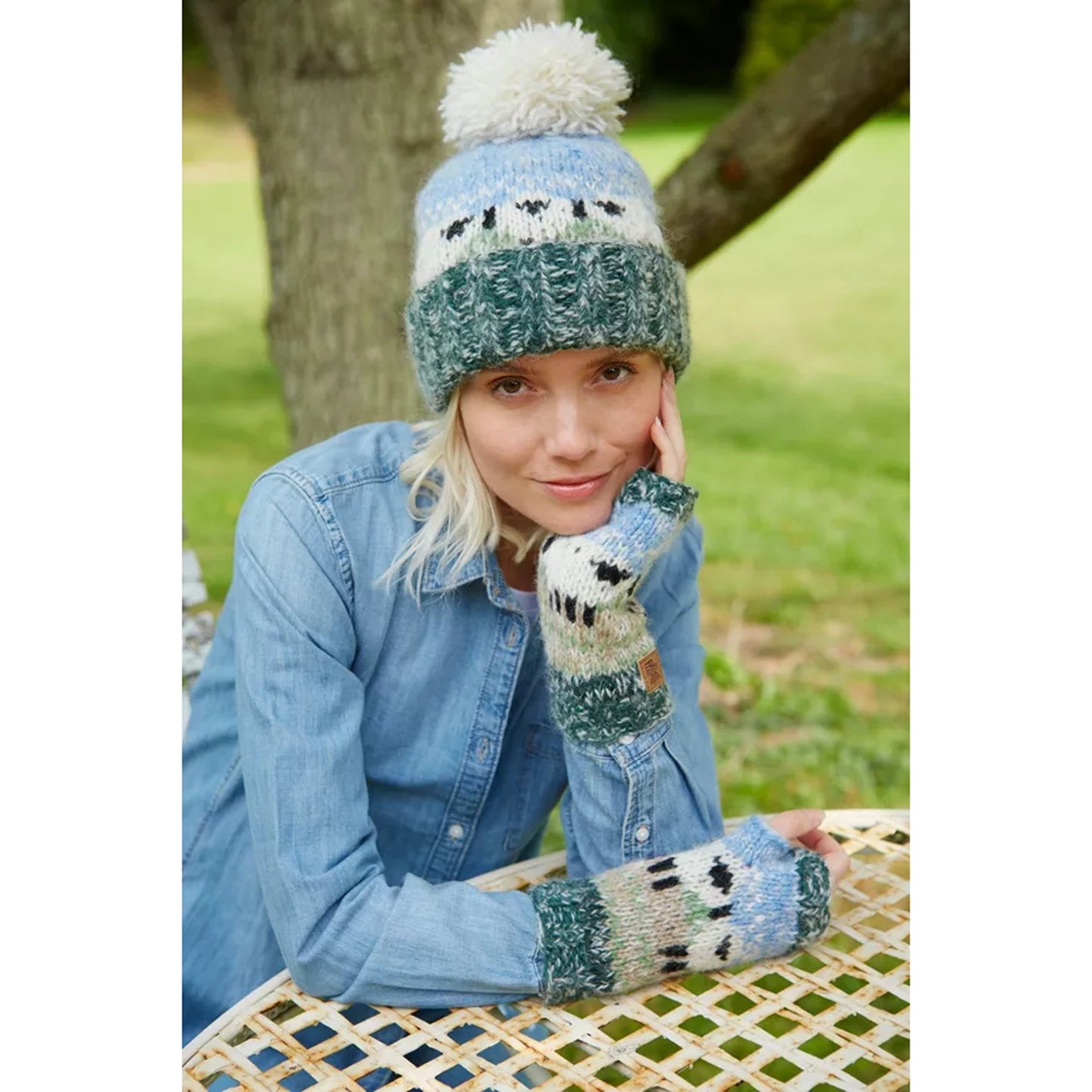 A model wearing a pair of knitted hand warmers featuring sheep in a field