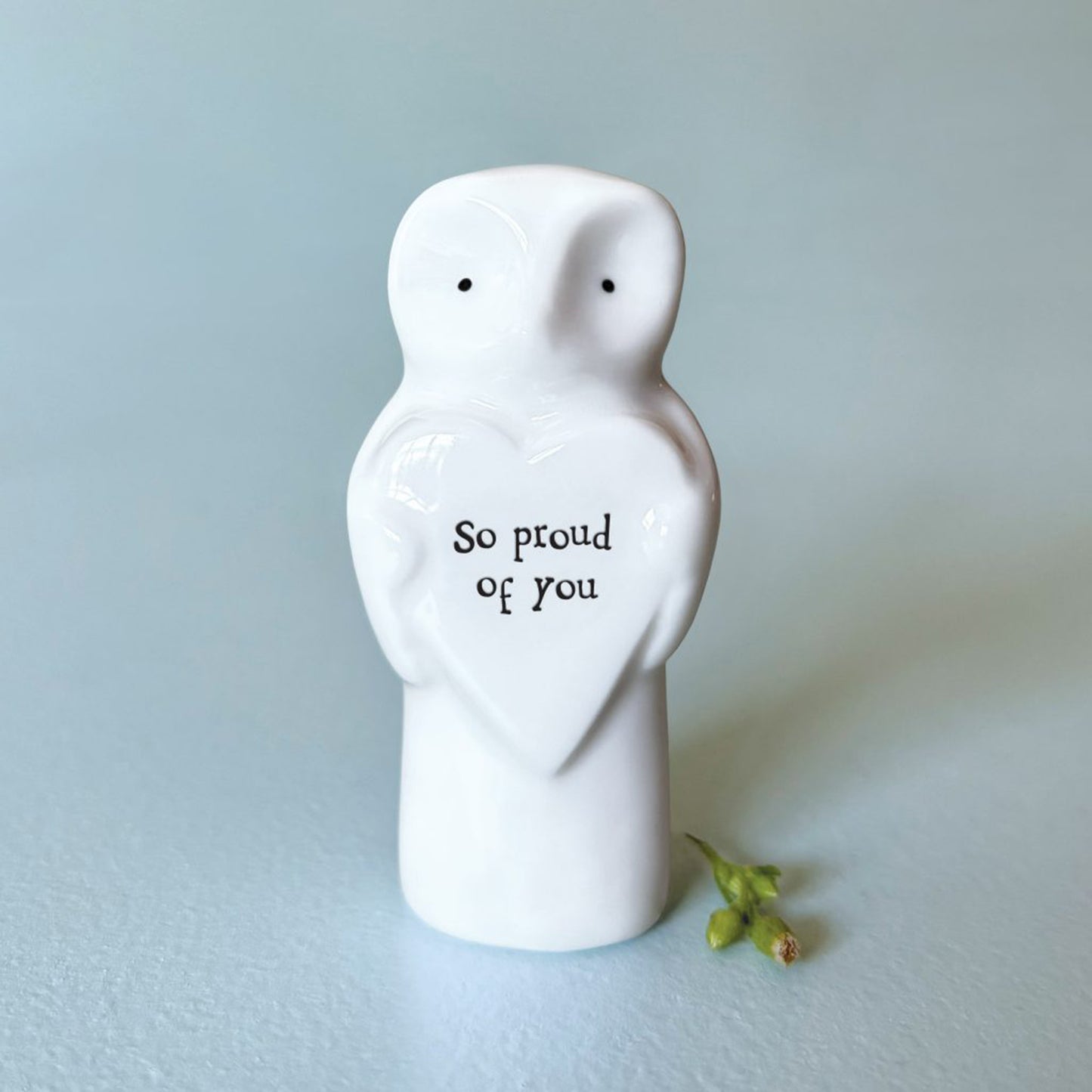 A owl figure holding a heart plaque with the words 'So proud of you'