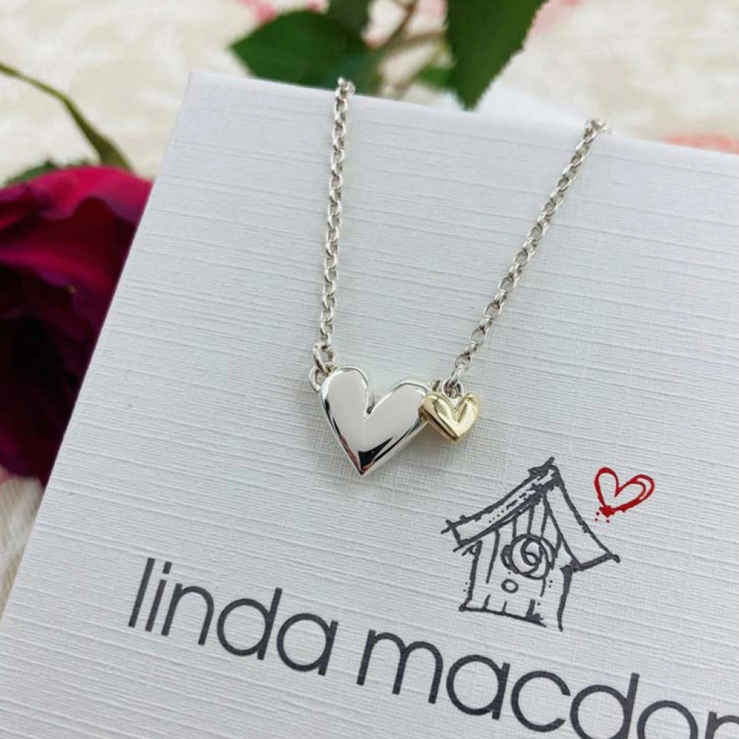 A silver heart necklace with a small gold heart drop charm on box