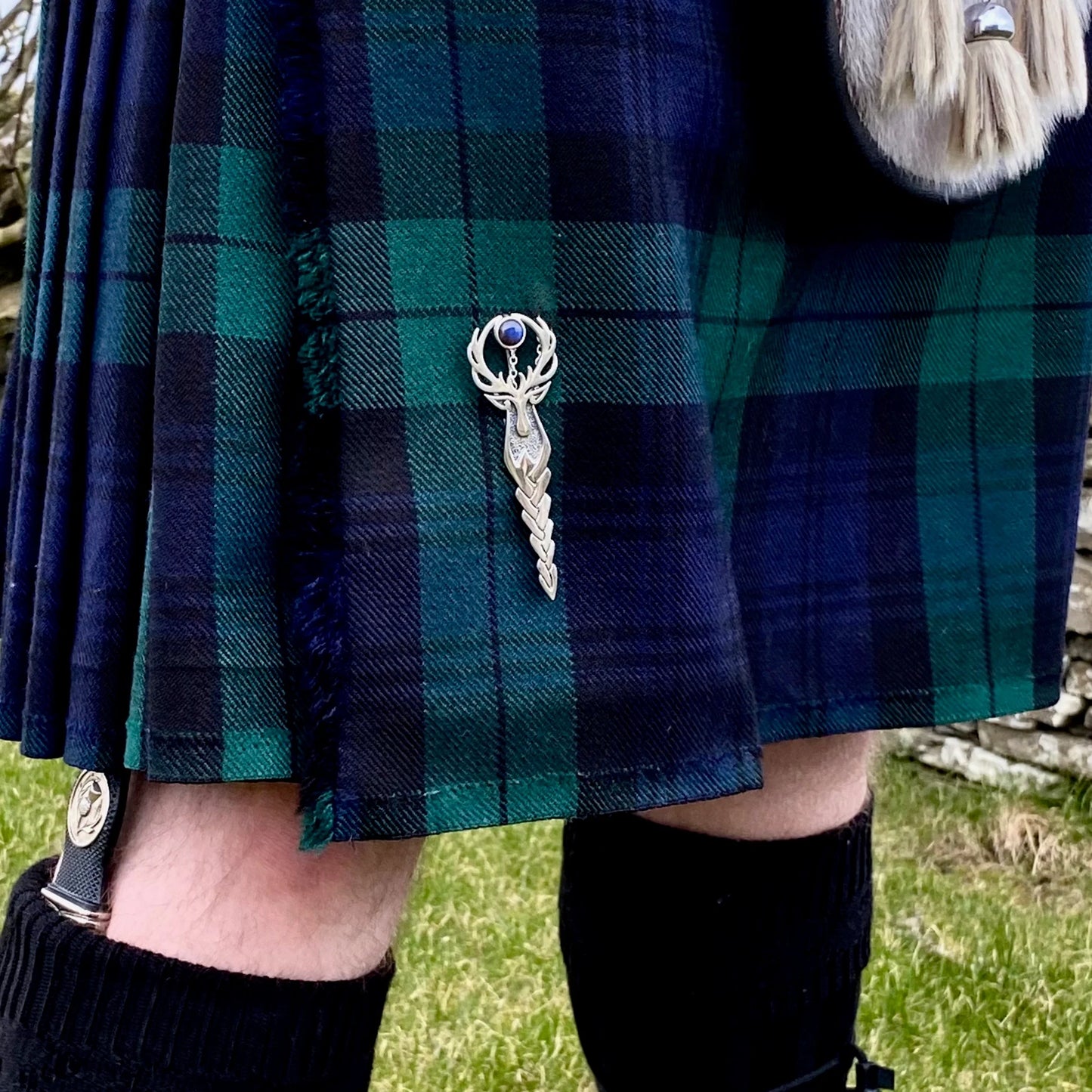 A stag pin with long Celtic braid and stag head top with amethyst stone shown worn on a kilt
