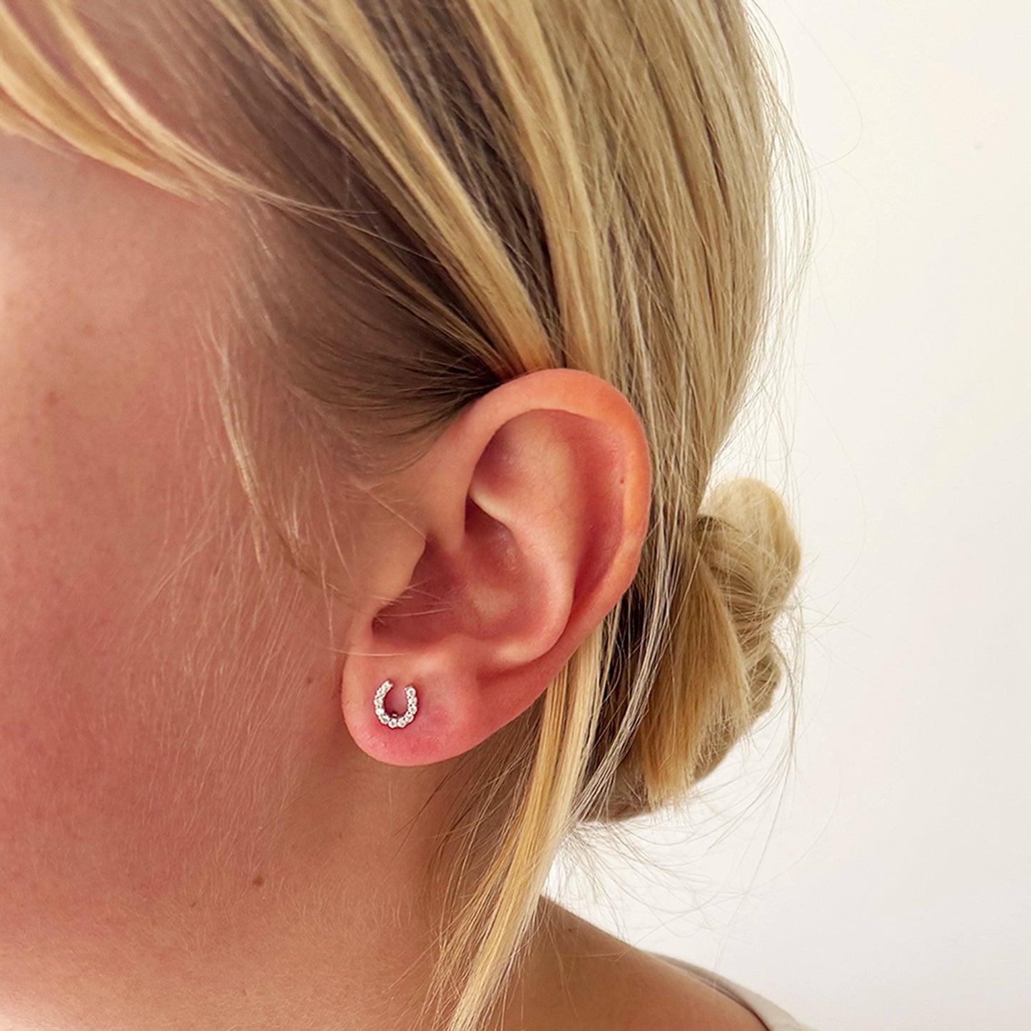 Model wearing silver stud earrings shaped like horseshoes with CZ stones