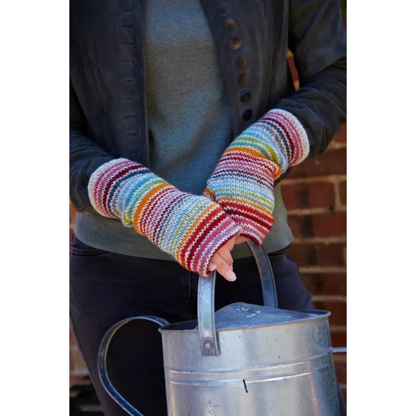Model wearing a pair of wool knitted wrist warmers with thin rainbow stripes on white