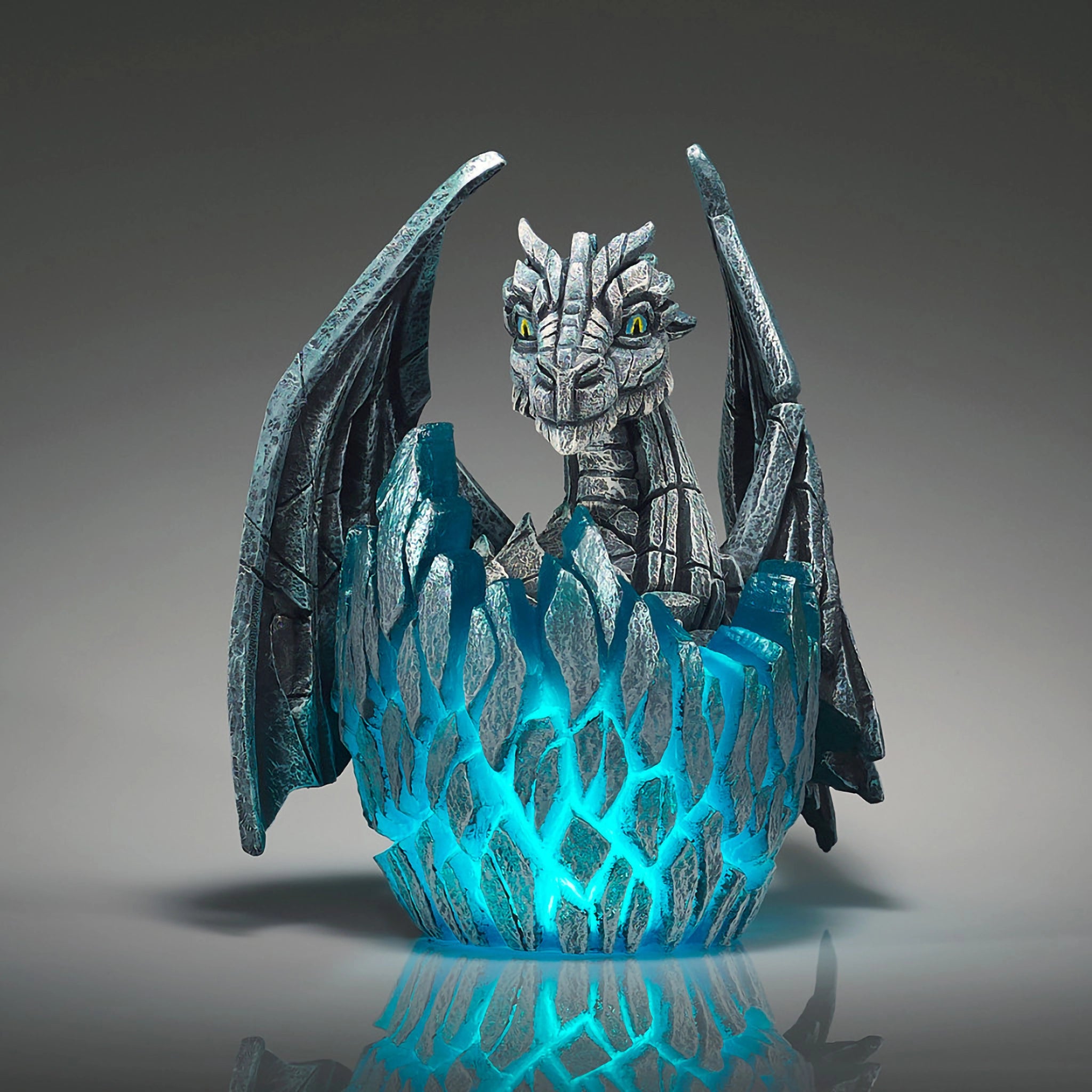 Front of a modern sculpture of a white baby dragon hatching from an egg that lights up in blue