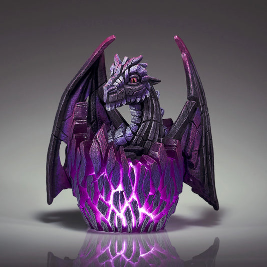 A modern sculpture of a black baby dragon hatching from an egg that lights up in purple