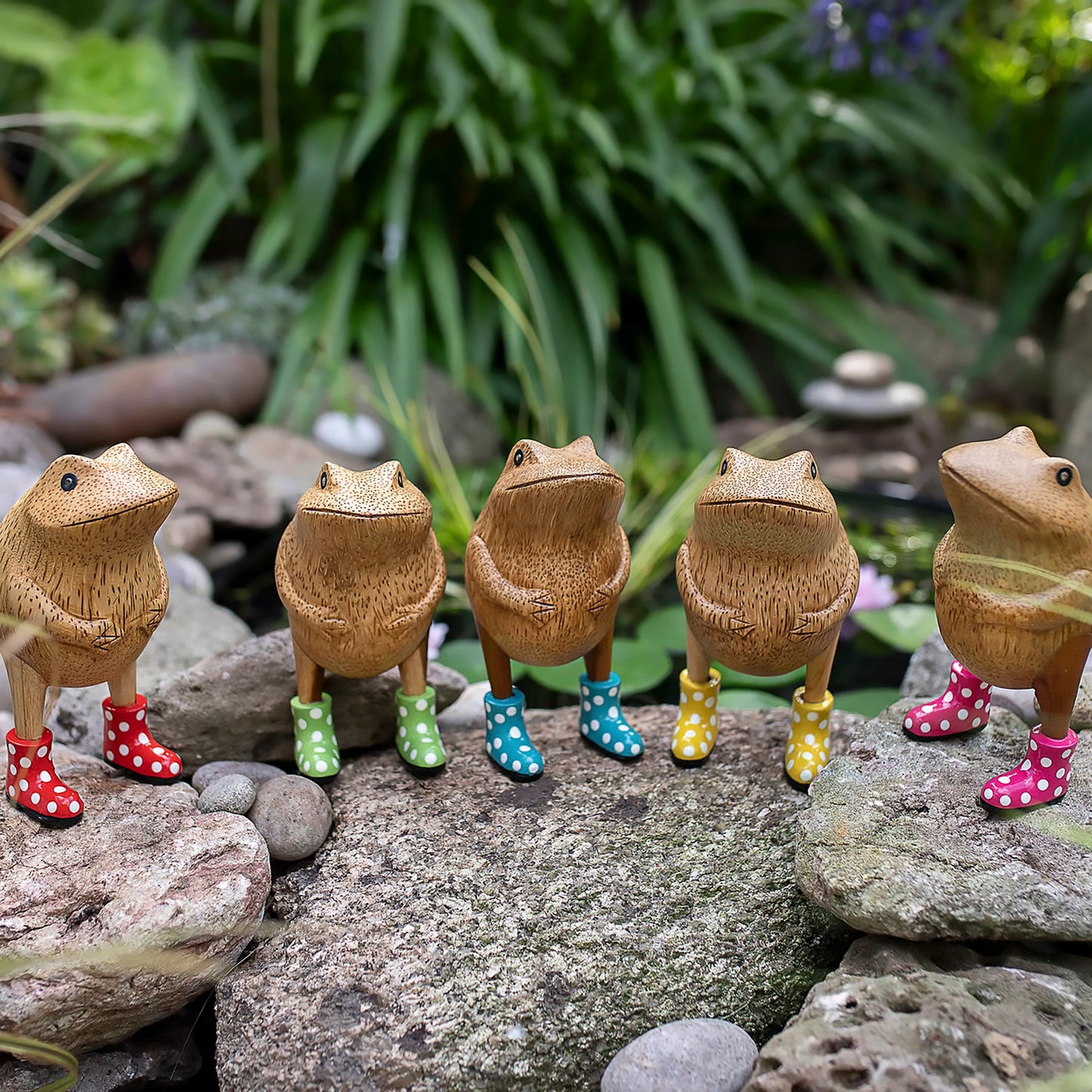 Wooden frog figurines with spotted wellies posed outside on rocks