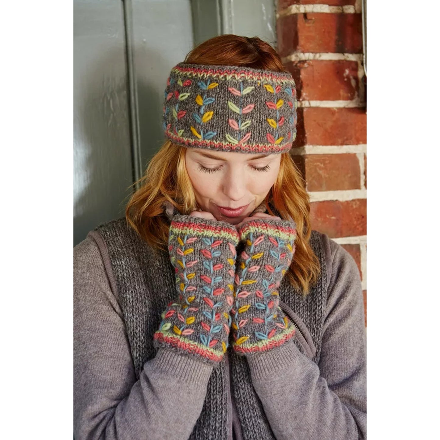 Model wearing a pair of knitted grey handwarmers with multicolour running leaf