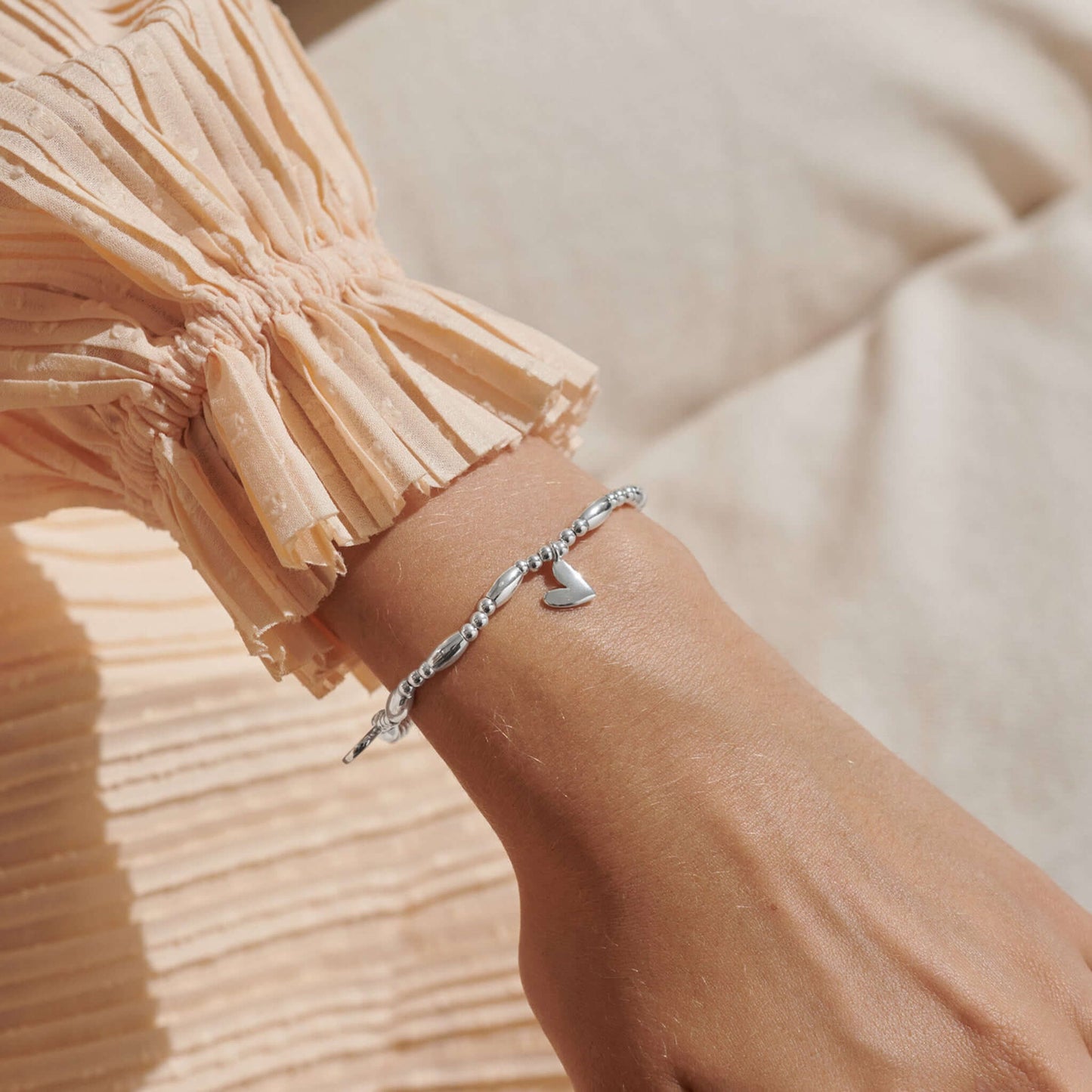 Model wearing a beaded stretch silver bracelet with three different heart charms