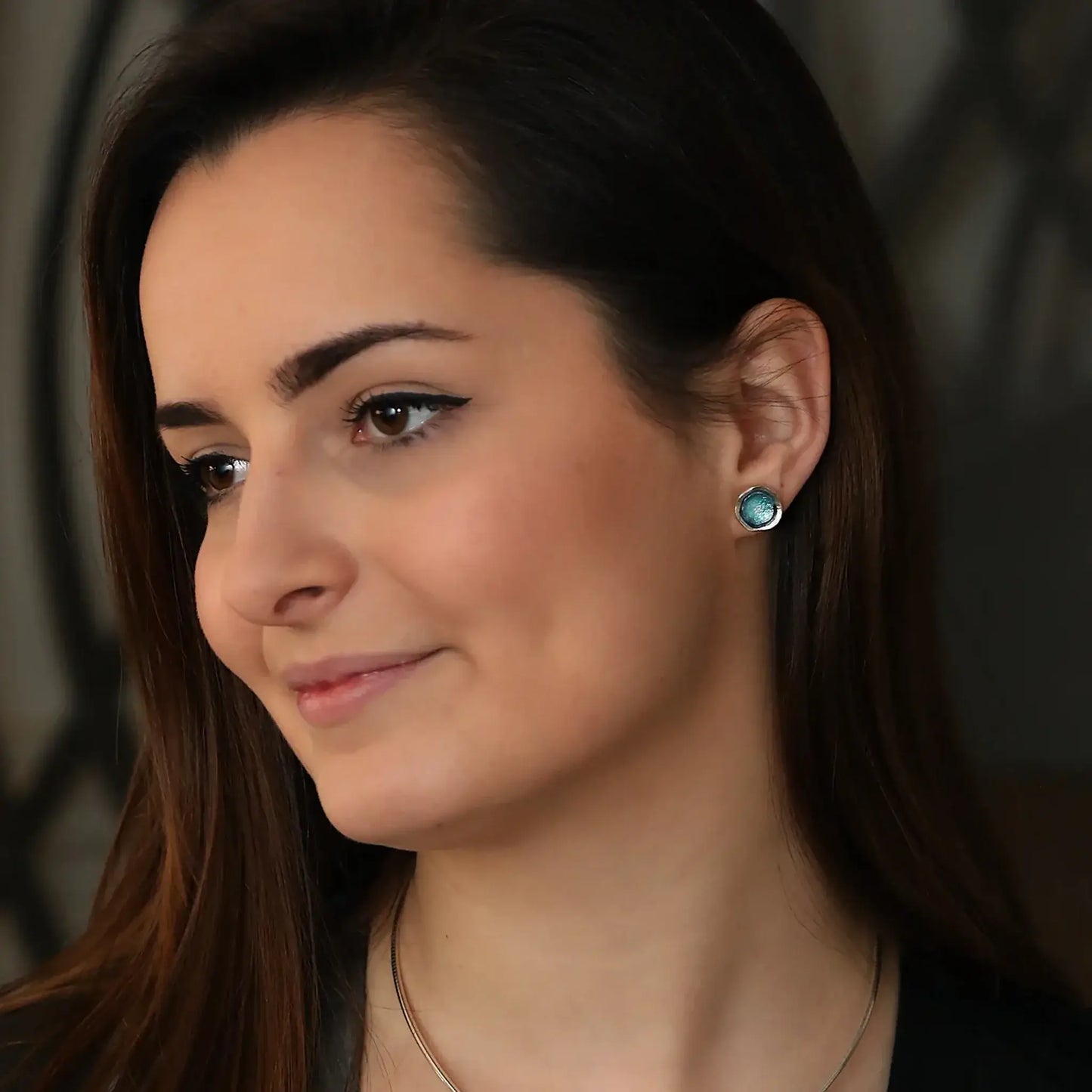 Model wearing silver round stud earrings with organic shape and subtle texture and blue green enamel centres