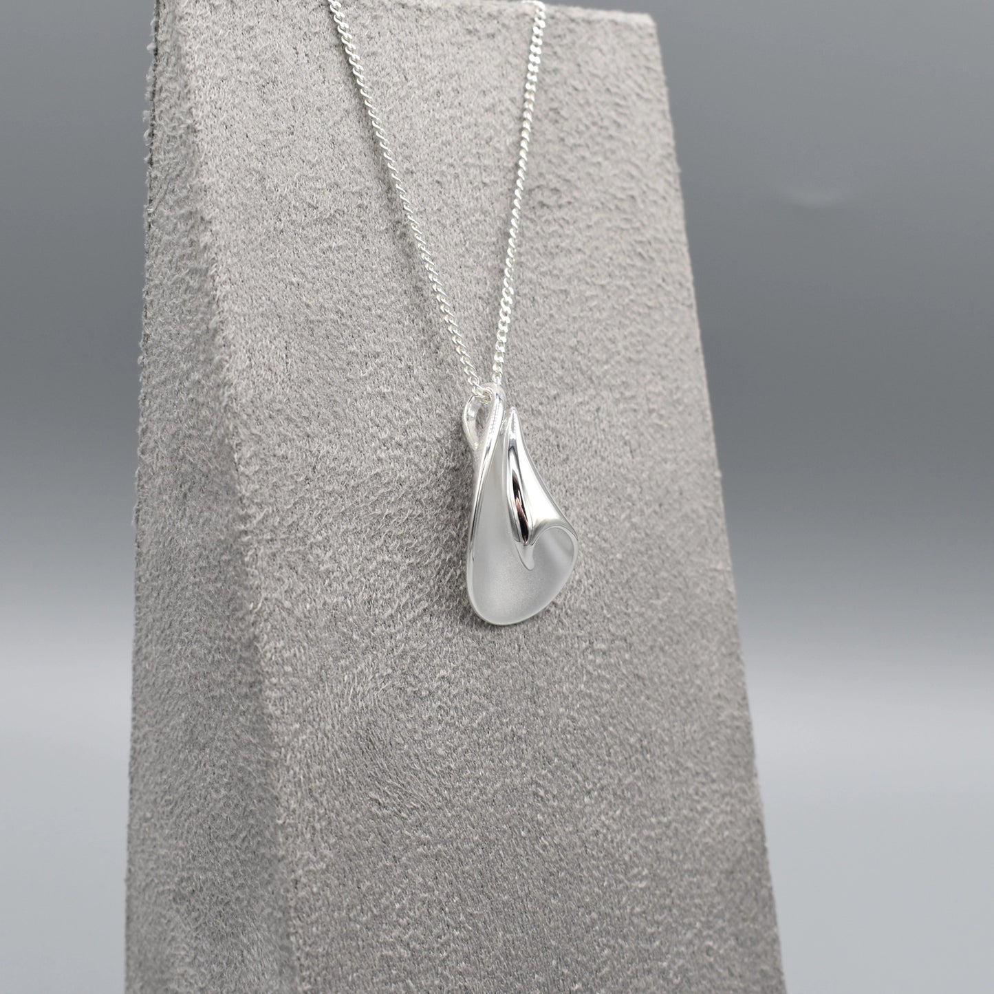 A curved pendant with a twist in a matt and polished silver finish on a silver chain side view