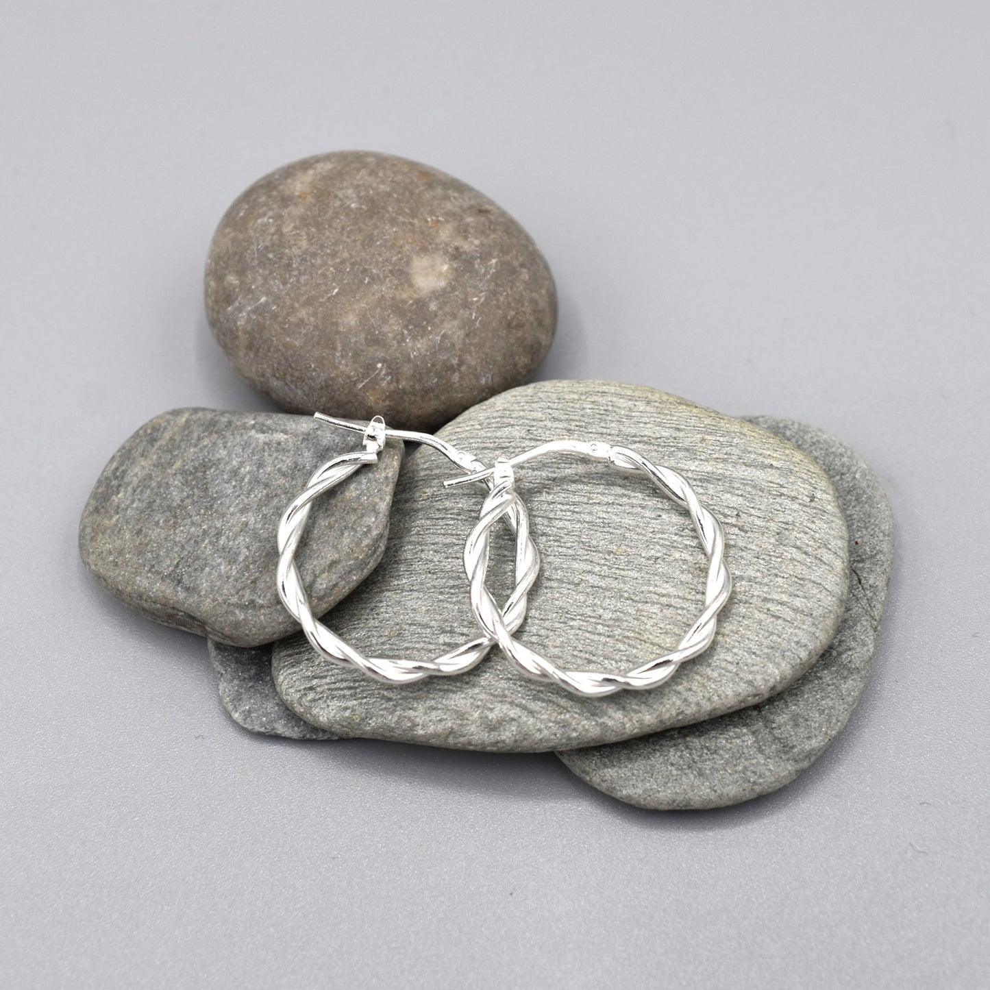 A pair of silver twist hoop earrings with hinge clasps