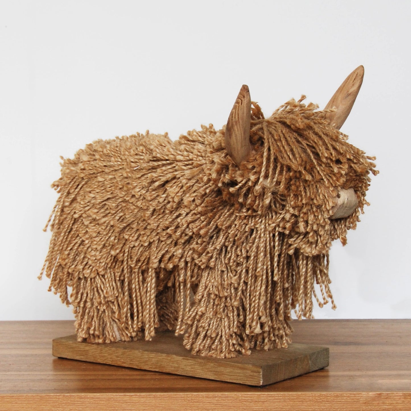 A full natural jute fiber Highland cow sculpture on a wood plank stand