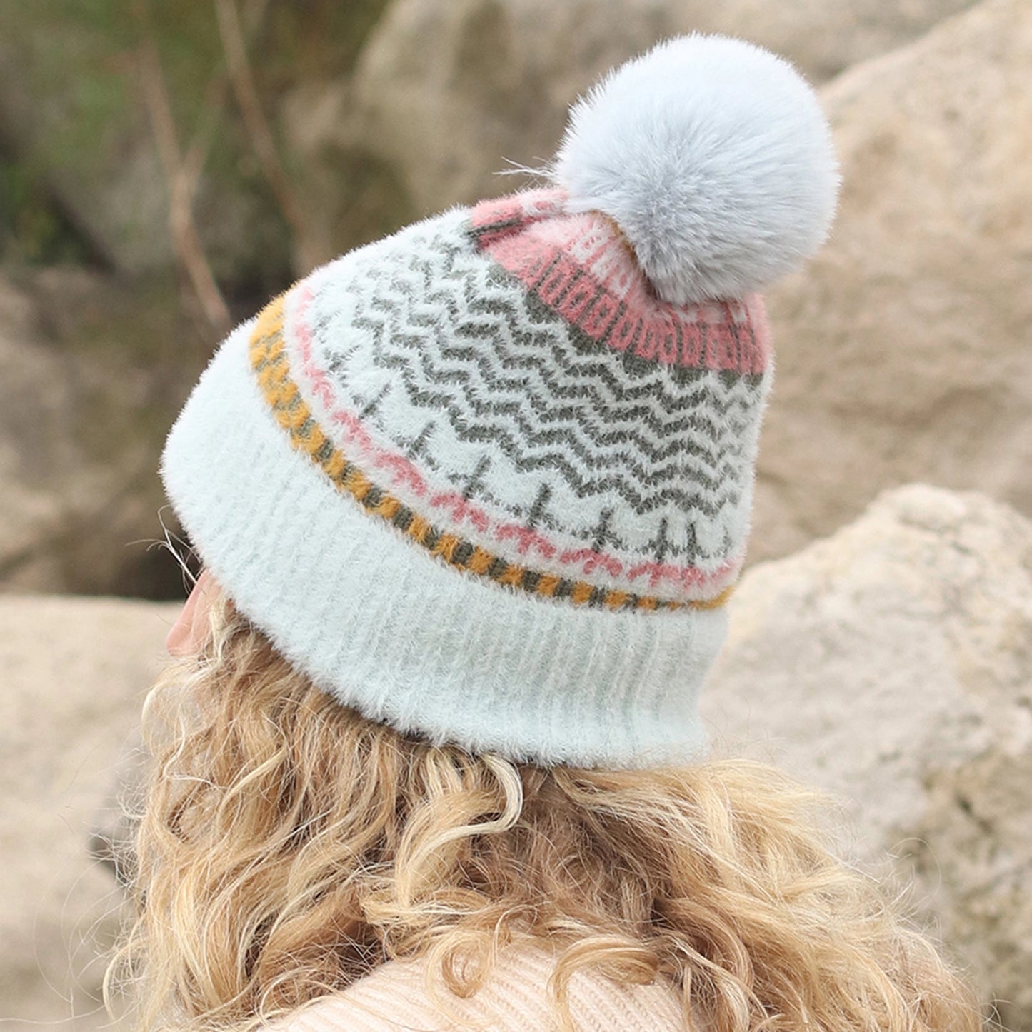 Model wearing multi patterned brushed knitted hat with faux fur pompom in aqua, pink and yellow back view